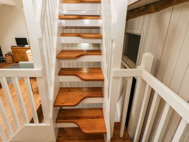 A wooden staircase with white railings in a house with a living room visible in the background at Bower Coach House in Bower Hinton near Martock