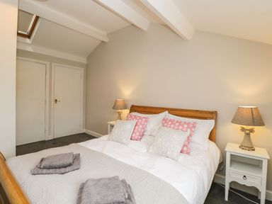 A bedroom with a wooden bed white bedding pink and white pillows bedside tables with lamps and folded towels on the bed at Bower Coach House in Bower Hinton near Martock