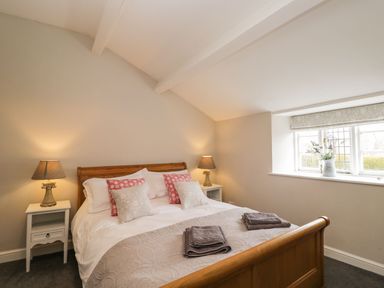 A bedroom with a wooden bed, two bedside tables with lamps, folded towels on the bed, and a window with a flower pot at Bower Coach House in Bower Hinton near Martock