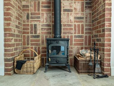 A wood stove with firewood baskets and tools at East Wing in Crewkerne