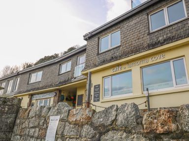 Exterior view of the cafe lamorna cove with stone wall in front and building with windows and signage