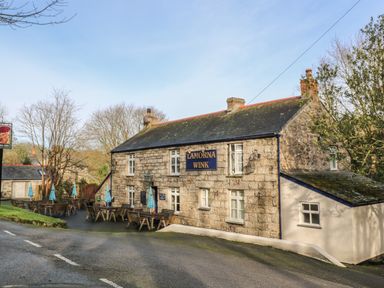 An outdoor seating area with tables and umbrellas next to a stone building with a sign reading Lamorna Wink in St Buryan