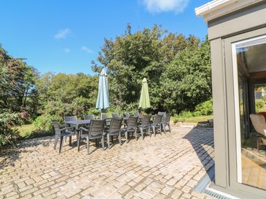 An outdoor patio with a long dining table surrounded by chairs and two closed umbrellas at Ros Vale in St Buryan