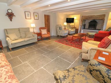 A living room with various chairs and sofas a red patterned rug a fireplace and a wall clock at Ros Vale in St Buryan