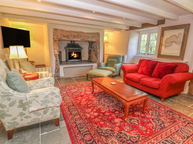 A living room with a fireplace red sofa green armchairs wooden coffee table and a red patterned rug at Ros Vale in St Buryan
