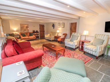 A living room with multiple sofas and armchairs a wooden coffee table and a red patterned rug at Ros Vale in St Buryan
