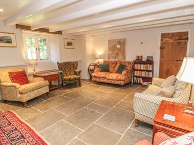 A sitting room with armchairs sofas side tables lamps bookshelf and a window at Ros Vale in St Buryan