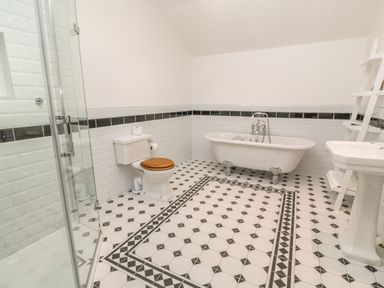 A bathroom with a clawfoot bathtub toilet with wooden seat shower with glass door and pedestal sink at Ros Vale in St Buryan