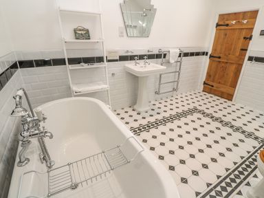 A bathroom with a freestanding bathtub a pedestal sink a wooden door and patterned floor tiles at Ros Vale in St Buryan
