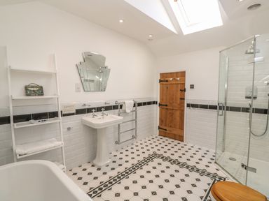 A bathroom with a white pedestal sink a wooden door a glass shower enclosure and a white shelf unit with towels and a small sign at Ros Vale in St Buryan