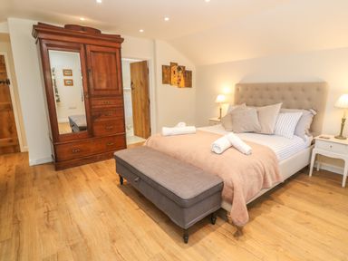 A bedroom with a bed cushions and a blanket a wardrobe a bench at the foot of the bed and bedside tables with lamps at Ros Vale in St Buryan