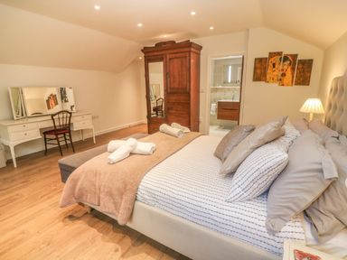 A bedroom with a bed pillows and folded towels a wooden wardrobe a white dressing table with a chair and a door leading to a bathroom at Ros Vale in St Buryan