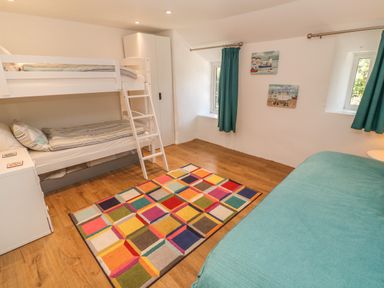 A bedroom with bunk beds a colorful rug a wardrobe and teal curtains at Ros Vale in St Buryan
