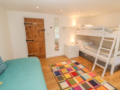 A bedroom with a wooden door a bunk bed a small chest of drawers a colorful rug and a turquoise couch at Ros Vale in St Buryan