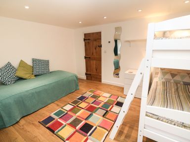 A bedroom with a green sofa bed three pillows bunk beds with ladder a multicolored rug wooden door and a wavy mirror at Ros Vale in St Buryan