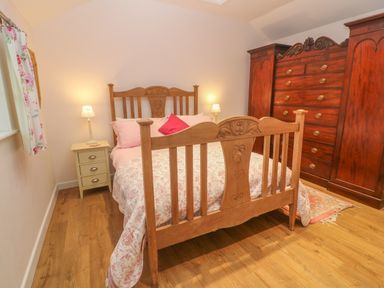 A bedroom with a wooden bed a bedside table with a lamp a large wooden wardrobe and a floral curtain at Ros Vale in St Buryan