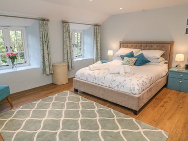 A bedroom with a bed, bedside tables, lamps, curtains, and a rug at Ros Vale in St Buryan