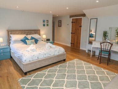 A bedroom with a large bed two blue bedside tables a wooden chair a white dressing table and a patterned rug at Ros Vale in St Buryan