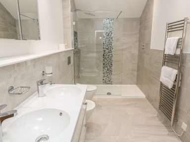 A bathroom with double sinks, a shower area with glass partition, a toilet, and a towel radiator with towels at Ros Vale in St Buryan