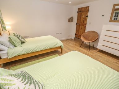 A bedroom with two single beds a wooden door a wicker chair and a white chest of drawers at Ros Vale St Buryan
