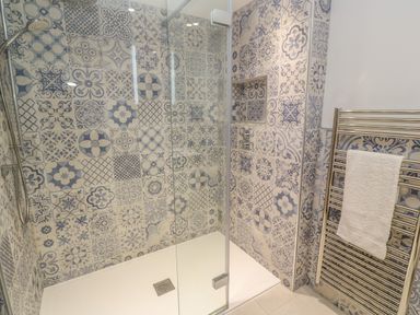 A shower area with blue patterned tiles and a glass door next to a towel radiator with a white towel at Ros Vale in St Buryan