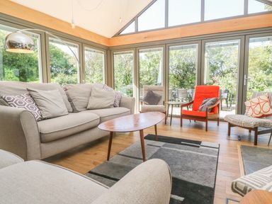 A living room with sofas chairs a coffee table and large windows overlooking a garden at Ros Vale in St Buryan