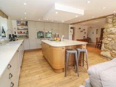 A kitchen with a central island with sink and stools a stone wall and wooden floor at Ros Vale in St Buryan