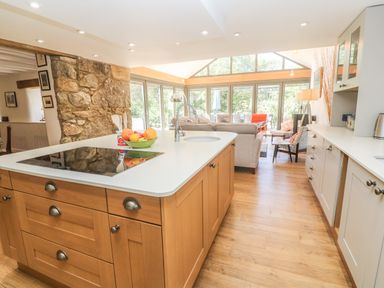 A kitchen with wooden cabinets and island next to a living area with sofa and chairs at Ros Vale in St Buryan