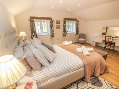 A bedroom with a bed with pillows and rolled towels two windows a chair and a dressing table at Ros Vale in St Buryan