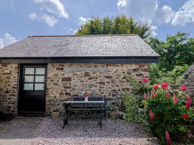 A garden with stone wall and table at The Old Workshop in Knowstone