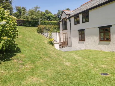 A grassy garden with a swing set and a patio area next to a two-story house at Meadow Lea in Pensilva near Liskeard