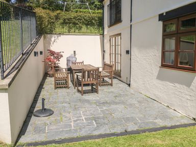 An outdoor patio with a wooden table and four chairs near a house with cream walls at Meadow Lea in Pensilva near Liskeard