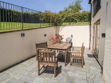 A patio with wooden table and chairs a barbecue grill and a small tree at Meadow Lea in Pensilva near Liskeard