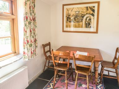 A dining area with a wooden table and four wooden chairs a wall painting and a window with floral curtains at Meadow Lea Pensilva near Liskeard