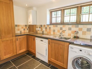 A kitchen with wooden cabinets a double sink dishwasher washing machine and tiled walls at Meadow Lea in Pensilva near Liskeard