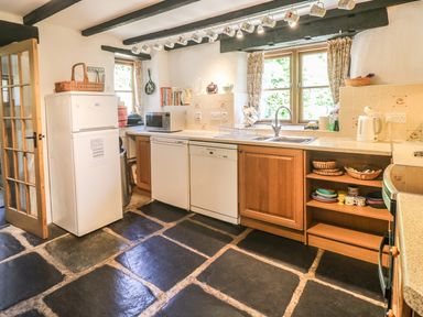 A kitchen with black stone floor wooden cabinets a white fridge microwave dishwasher sink and mugs hanging from ceiling at Meadow Lea in Pensilva near Liskeard