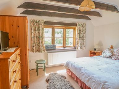 A bedroom with wooden furniture a bed window with floral curtains and a small green stool at Meadow Lea in Pensilva near Liskeard