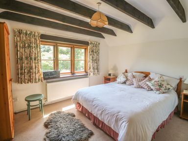 A bedroom with a double bed with floral and checkered cushions wooden furniture and a window with floral curtains at Meadow Lea Pensilva near Liskeard