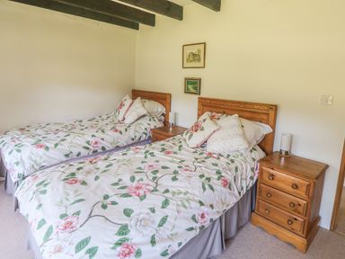 A bedroom with two single beds with floral bedspreads wooden headboards wooden bedside tables and framed pictures on the wall at Meadow Lea in Pensilva near Liskeard