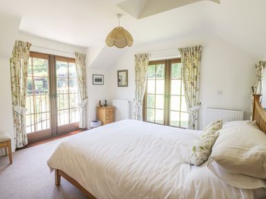 A bedroom with a large bed two sets of double doors with floral curtains a wooden bedside table and a hanging light at Meadow Lea Pensilva near Liskeard