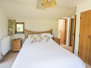 A bedroom with a bed with floral pillows two wooden nightstands and wooden doors at Meadow Lea in Pensilva near Liskeard