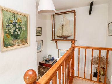 A staircase landing with wooden railing model ship in a glass case paintings and ceramic pots at Meadow Lea in Pensilva near Liskeard