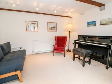A room with a black piano and bench a red armchair a dark sofa wall paintings and a floor lamp at Meadow Lea in Pensilva near Liskeard