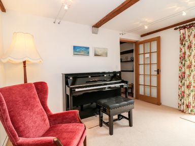 A room with a black upright piano and a matching bench red armchair a tall lamp wooden door and floral curtains at Meadow Lea Pensilva near Liskeard