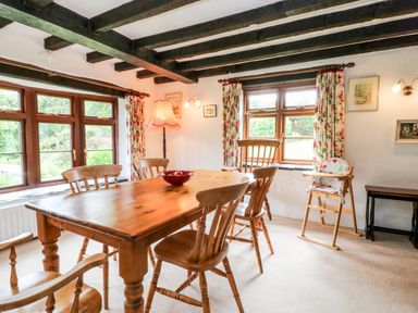 A dining room with a wooden table and chairs near windows with floral curtains at Meadow Lea Pensilva near Liskeard