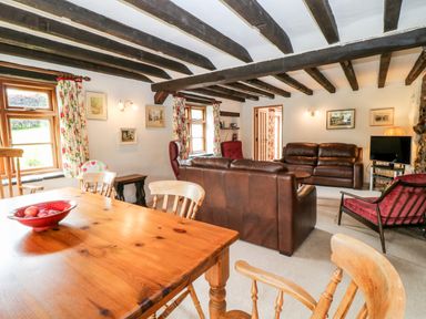 A living room and dining area with wooden table chairs leather sofas and exposed wooden beams at Meadow Lea in Pensilva near Liskeard