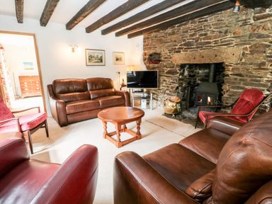 A living room with leather sofas stone fireplace wooden beams and a television at Meadow Lea in Pensilva near Liskeard