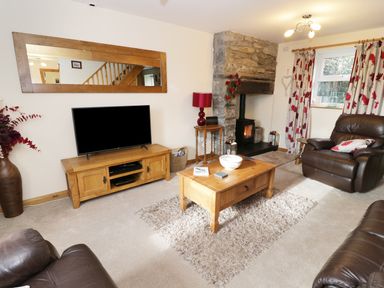 A living room with a television on a wooden stand a coffee table on a rug leather armchairs a stone fireplace and patterned curtains at 60 Hyfrydle Road Talysarn near Caernarfon