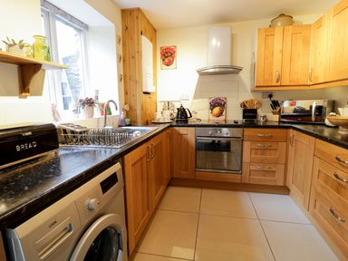 A kitchen with wooden cabinets a washing machine a stainless steel sink an oven microwave and various kitchen utensils at 60 Hyfrydle Road Talysarn near Caernarfon