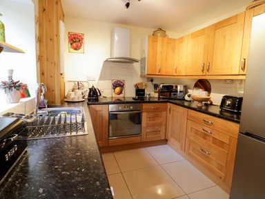 A kitchen with wooden cabinets, black countertops, a stove, a microwave, a toaster, and a sink at 60 Hyfrydle Road Talysarn near Caernarfon